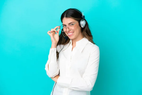Telemarketer Italian woman working with a headset isolated on blue background with glasses and happy