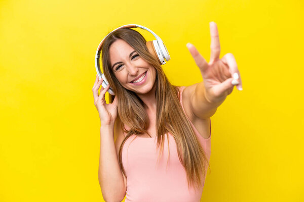 Young caucasian woman isolated on yellow background listening music and singing