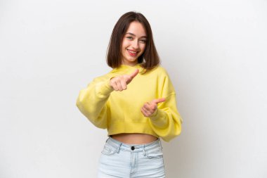 Beyaz arka planda izole edilmiş genç Ukraynalı kadın ön tarafı işaret ediyor ve gülümsüyor.