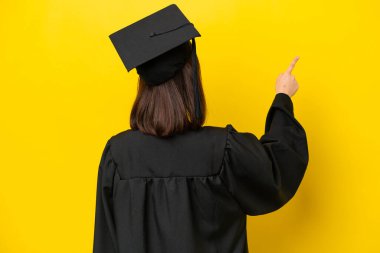 Genç üniversite mezunu, sarı arka planda izole edilmiş Ukraynalı kadın işaret parmağıyla işaret ediyor.