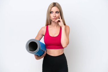 Genç sarışın kadın yoga derslerine giderken beyaz arka planda izole edilmiş bir minder tutuyor. Şüpheleri ve düşünceleri var.