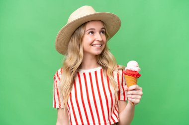 Young English woman with a cornet ice cream over isolated background looking up while smiling