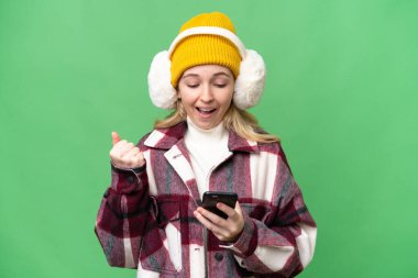 Young  English woman wearing winter muffs over isolated background surprised and sending a message