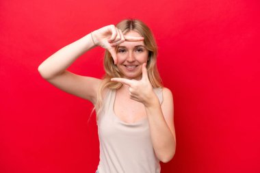 Young English woman isolated on red background focusing face. Framing symbol
