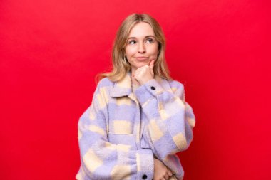 Genç İngiliz kadın, kırmızı arka planda izole edilmiş bir şekilde yukarı bakarken bir fikir düşünüyor.