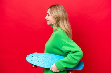 Genç bir İngiliz kadın, kırmızı arka planda tek başına paten kayıyor.