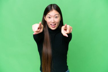 Genç Asyalı kadın izole edilmiş krom anahtar arka planı şaşırmış ve ön tarafı işaret ediyor.