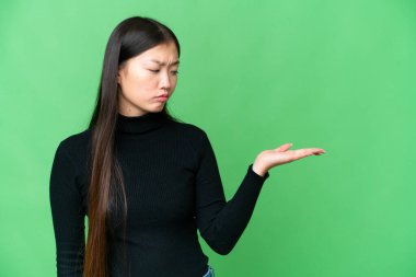 Young Asian woman over isolated chroma key background holding copyspace with doubts