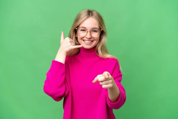 Young English woman over isolated background making phone gesture and pointing front