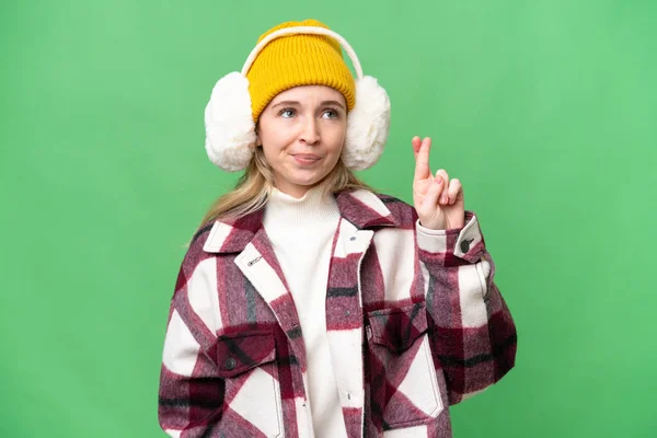 Young  English woman wearing winter muffs over isolated background with fingers crossing and wishing the best