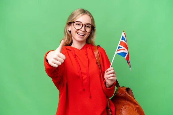 Young hispanic woman holding an United Kingdom flag over isolated background with thumbs up because something good has happened