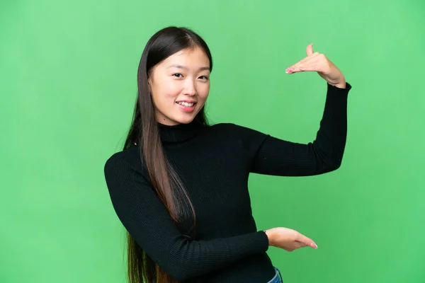 Young Asian woman over isolated chroma key background holding copyspace to insert an ad