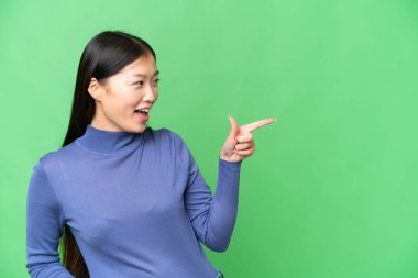 Young Asian woman over isolated chroma key background pointing finger to the side and presenting a product