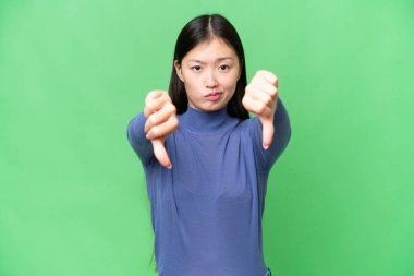 Young Asian woman over isolated chroma key background showing thumb down with two hands