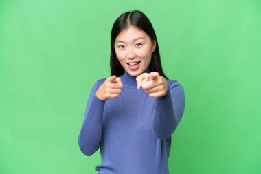 Genç Asyalı kadın izole edilmiş krom anahtar arka planı şaşırmış ve ön tarafı işaret ediyor.