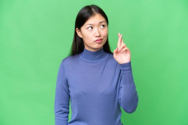 Young Asian woman over isolated chroma key background with fingers crossing and wishing the best