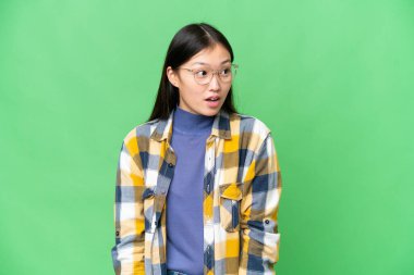 Genç Asyalı bir kadın izole edilmiş krom anahtar geçmişi var. Yan tarafa bakarken sürpriz jest yapıyor.