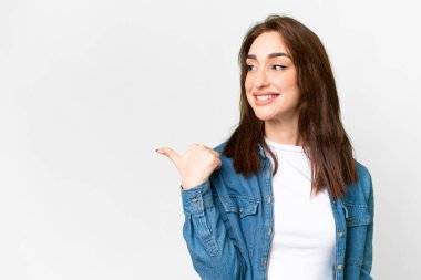 İzole edilmiş beyaz arka planda genç beyaz kadın bir ürünü sunmak için kenarı işaret ediyor.