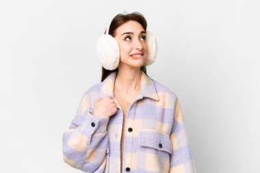 Young caucasian woman wearing winter muffs over isolated white background and looking up