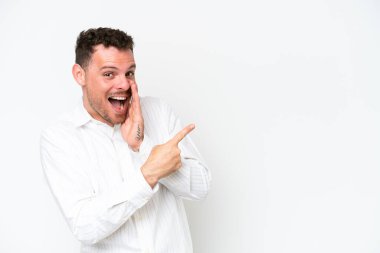 Beyaz arka planda soyutlanmış beyaz tenli yakışıklı bir adam bir ürün sunmak ve bir şeyler fısıldamak için kenarı işaret ediyor.