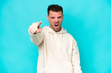 Kafkasyalı yakışıklı adam mavi arka planda izole edilmiş hayal kırıklığına uğramış ve ön tarafı işaret ediyor.