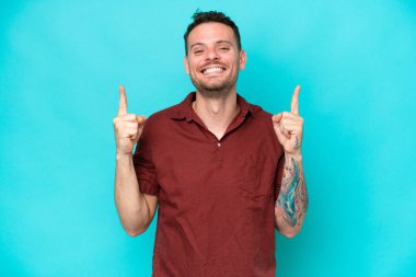 Mavi arka planda izole edilmiş beyaz, yakışıklı genç adam harika bir fikre işaret ediyor.