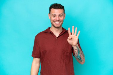 Genç, beyaz, yakışıklı bir adam mavi arka planda izole edilmiş mutlu ve parmaklarıyla dört kişi sayıyor.