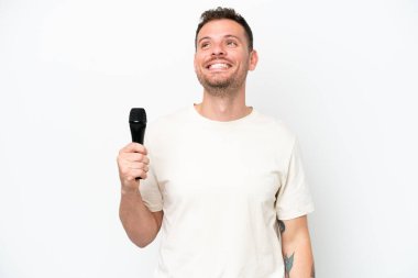 Young caucasian singer man picking up a microphone isolated on white background thinking an idea while looking up