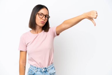 Beyaz arka planda izole edilmiş genç beyaz kadın olumsuz ifade ile baş parmağını aşağı gösteriyor.