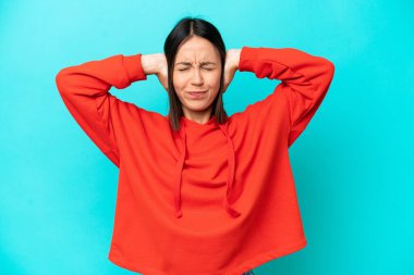 Mavi arka planda izole edilmiş genç beyaz kadın hayal kırıklığına uğramış ve kulaklarını kapatmış.