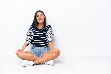 Beyaz arka planda izole bir şekilde yerde oturan beyaz bir kadın gülüyor.