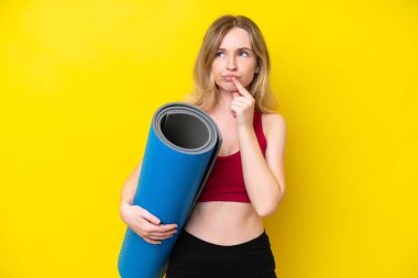 Young sport caucasian woman going to yoga classes while holding a mat isolated on yellow background having doubts while looking up
