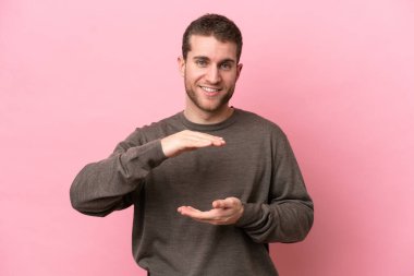 Pembe arka planda izole edilmiş genç beyaz bir adam bir ilan vermek için avucunun içinde hayali bir fotokopi makinesi tutuyor.