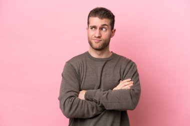 Young caucasian man isolated on pink background making doubts gesture while lifting the shoulders