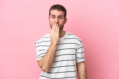 Pembe arka planda izole edilmiş, ağzı elle kaplanmış genç beyaz bir adam.
