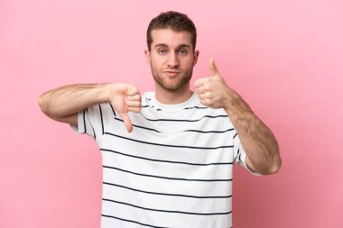 Pembe arka planda izole edilmiş beyaz bir adam iyiye-kötüye işaret yapıyor. Evet ya da hayır arasında kararsız