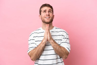 Pembe arka planda izole edilmiş genç beyaz adam avuç içlerini bir arada tutuyor. İnsan bir şey ister.