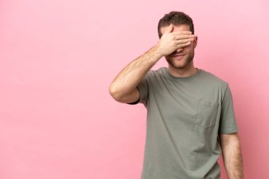 Pembe arka planda izole edilmiş genç, beyaz bir adam gözlerini elleriyle kapatıyor. Bir şey görmek istemiyorum.
