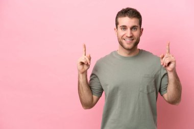 Pembe arka planda izole edilmiş genç beyaz adam harika bir fikre işaret ediyor.