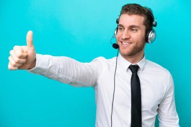 Tele pazarlamacı beyaz bir adam mavi arka planda izole edilmiş bir kulaklıkla çalışıyor.