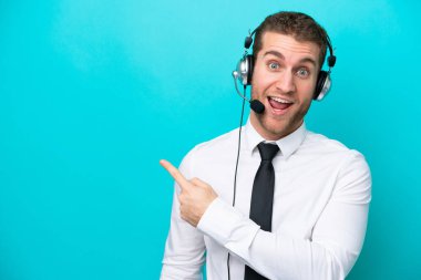 Tele pazarlamacı beyaz adam mavi arka planda izole edilmiş bir kulaklıkla çalışıyor.