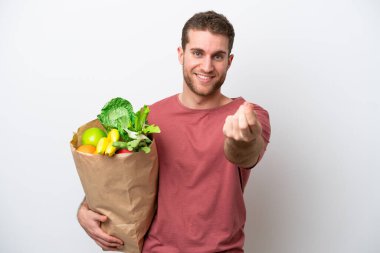 Young caucasian man holding a grocery shopping bag isolated on white background making money gesture