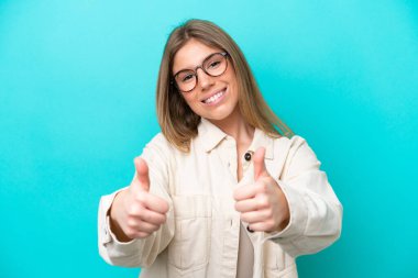 Mavi arka planda, gözlüklü ve baş parmağıyla izole edilmiş beyaz bir kadın.