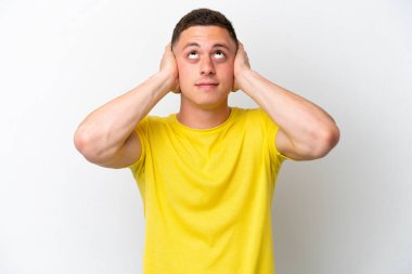 Beyaz arka planda izole edilmiş genç Brezilyalı adam hayal kırıklığına uğramış ve kulaklarını kapatmış.