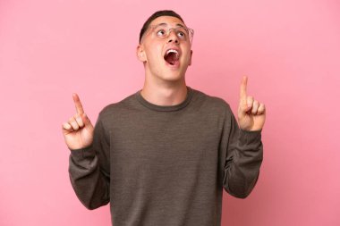Pembe arka planda izole edilmiş genç Brezilyalı adam şaşırmış ve işaret ediyor.