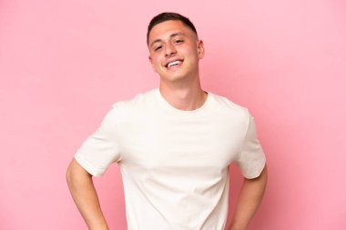 Pembe arka planda izole edilmiş genç Brezilyalı adam kolları kalçasında ve gülümsüyor.