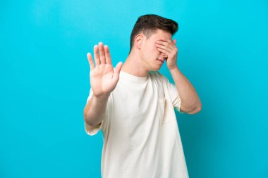 Young handsome Brazilian man isolated on blue background making stop gesture and covering face