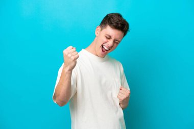 Genç yakışıklı Brezilyalı adam mavi arka planda izole edilmiş zaferi kutluyor.