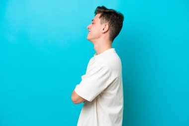 Young handsome Brazilian man isolated on blue background in lateral position