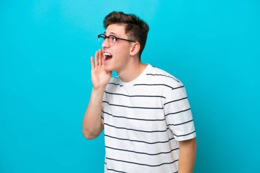 Young handsome Brazilian man isolated on blue background shouting with mouth wide open to the side